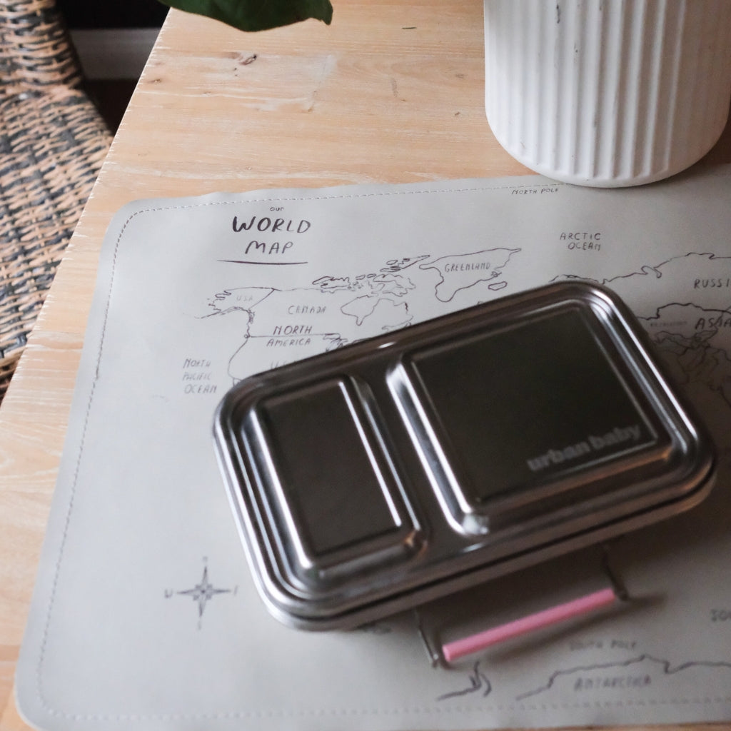 Stainless Steel 2 compartments  lunch box on a world map placemat with a white vase in the background